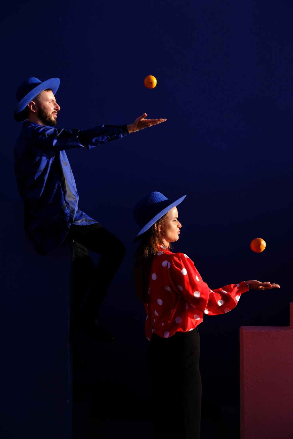 Adriana juggling an apple in a red polka dot blouse against the deep blue walls of Muralla Roja