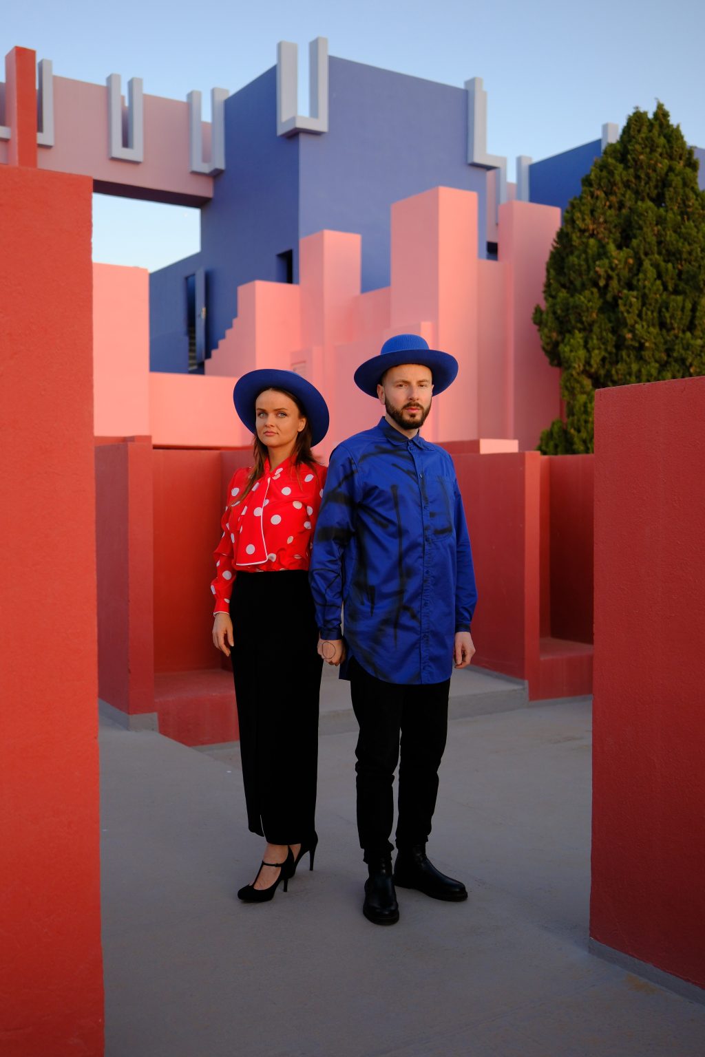 Portrait of Adriana and Ondrej in red and blue against the pink walls of Muralla Roja