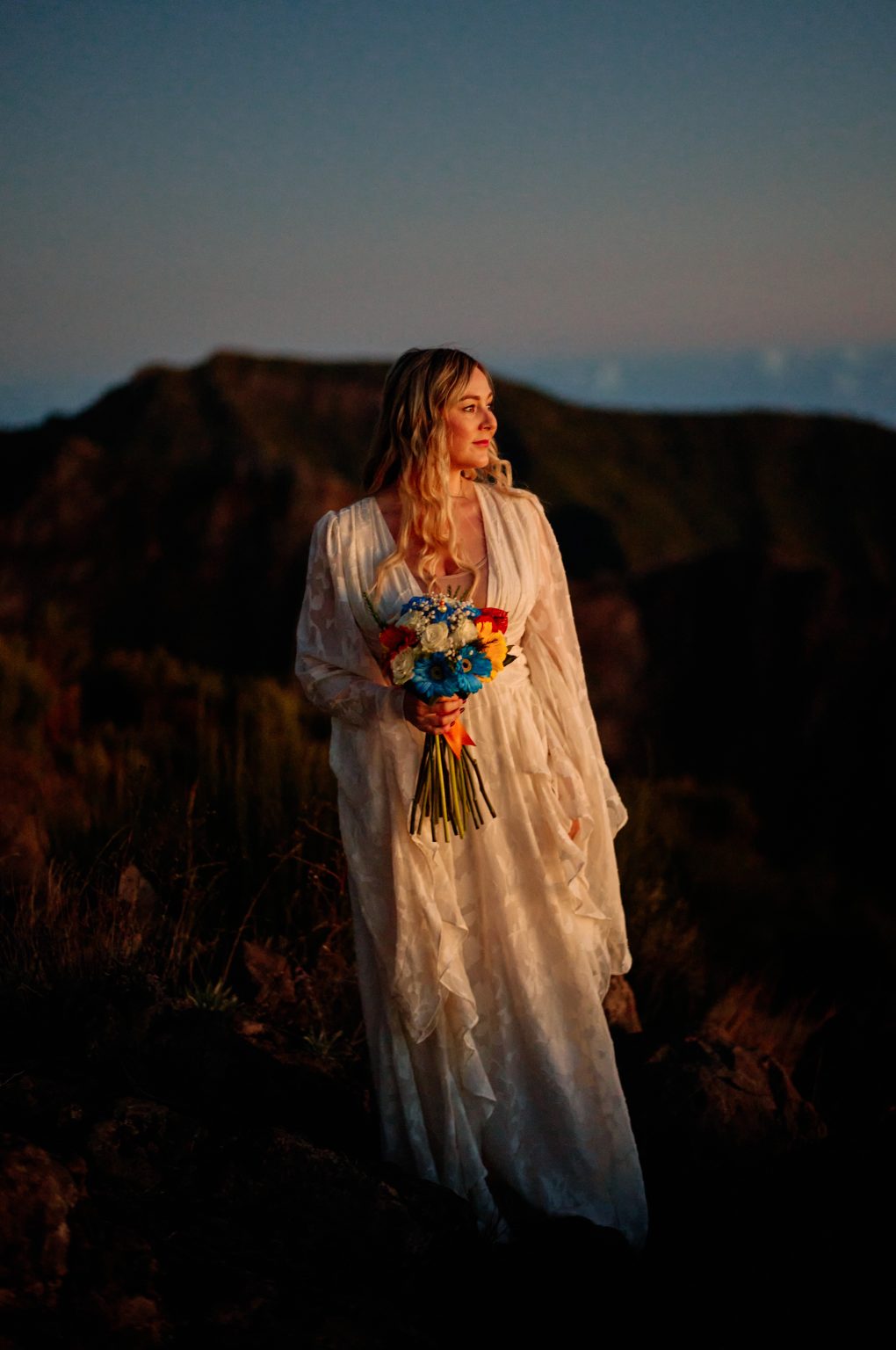 Bride in a lace dress holding a bright bouquet at sunrise, Pico do Arieiro, Madeira