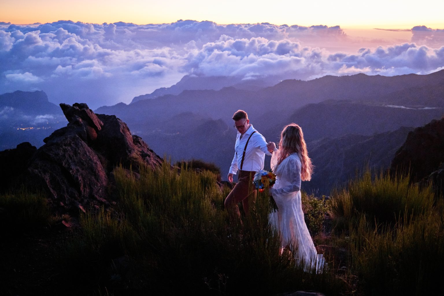Couple walking a grassy ridge above misty mountains at dawn, Madeira