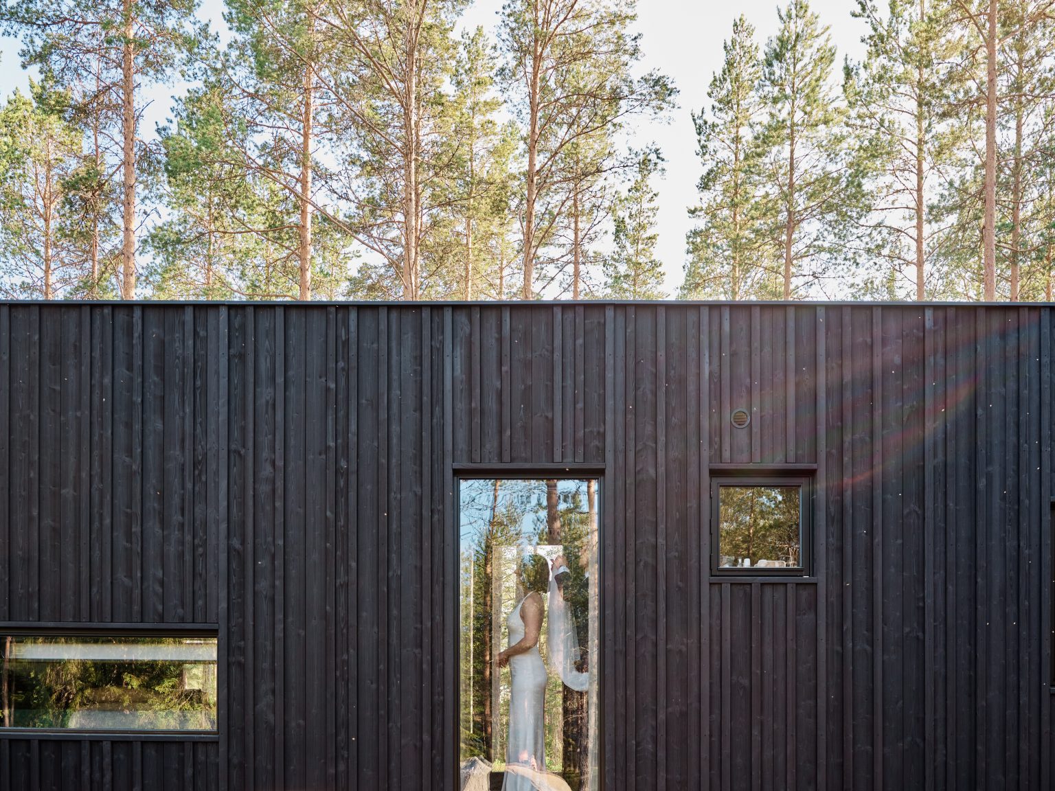 The black timber cabin at Hop Farm Beach with the bride in the doorway, Sweden