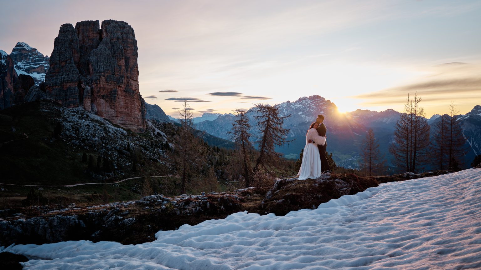 Elisa and Hector walking below the Cinque Torri towers at sunrise, snow on the ground in the Dolomites