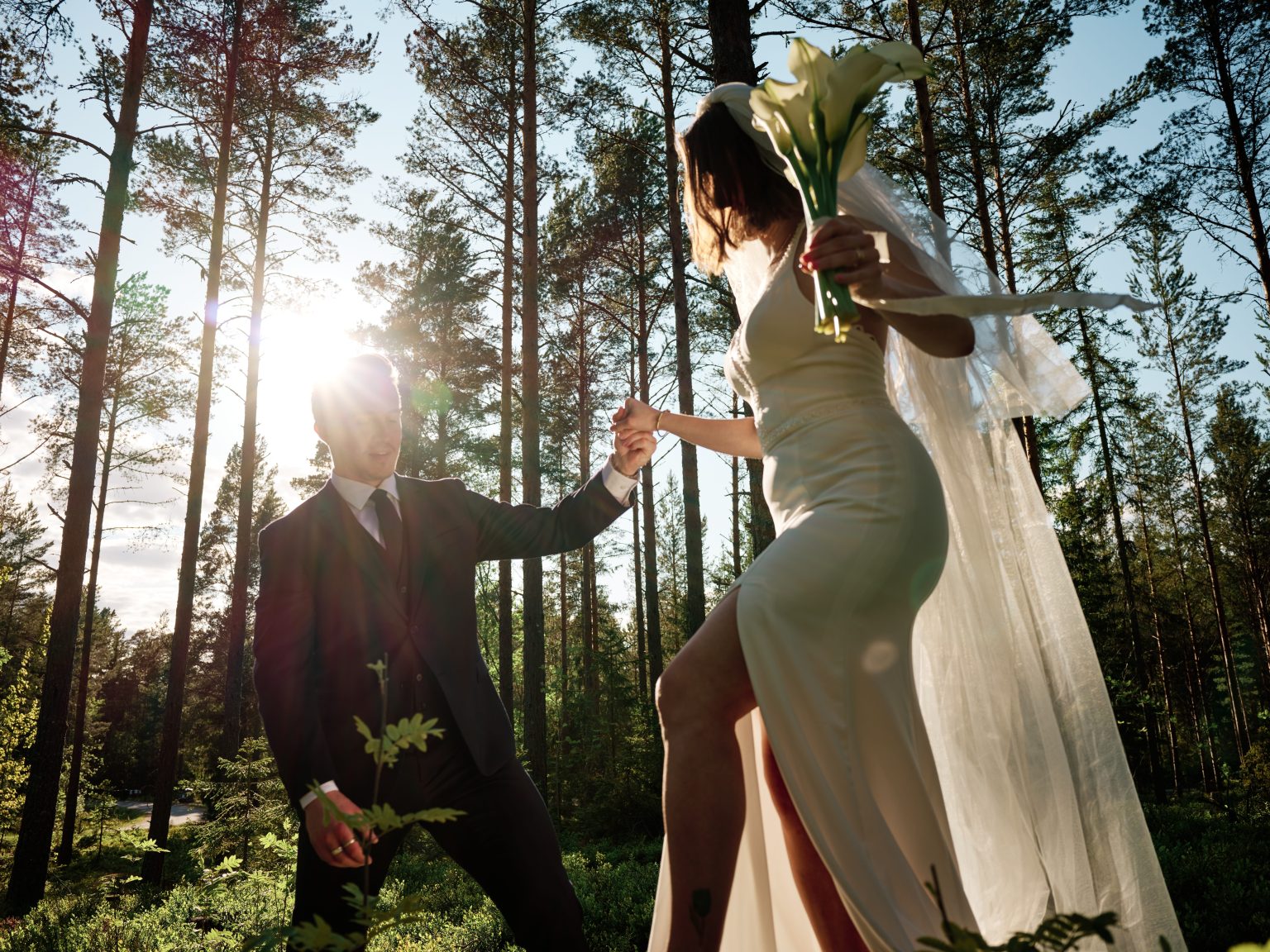 Martin leading Sara by the hand through the backlit pines