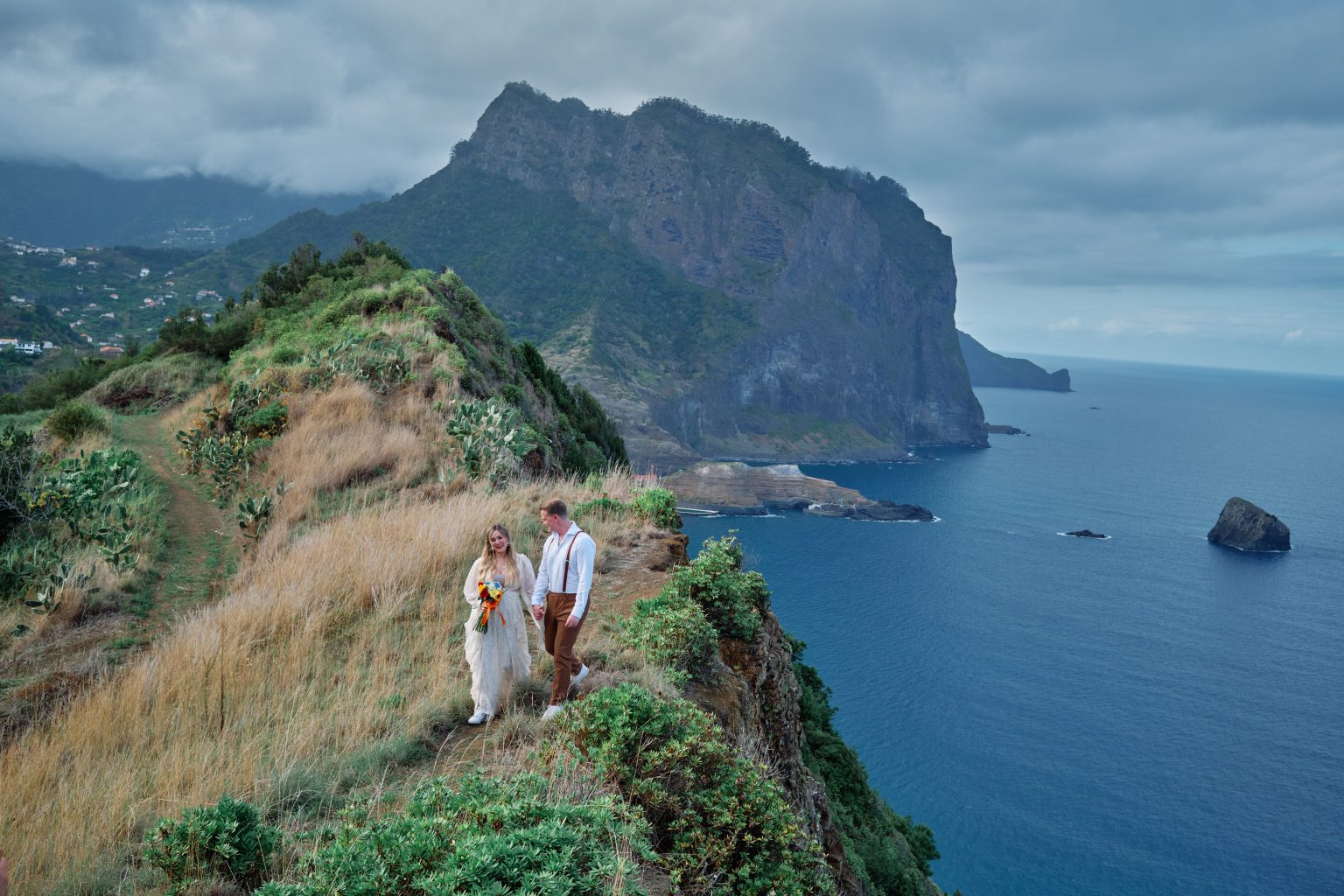 Couple walking a green clifftop path above the sea at Ponta de Sao Lourenco, Madeira