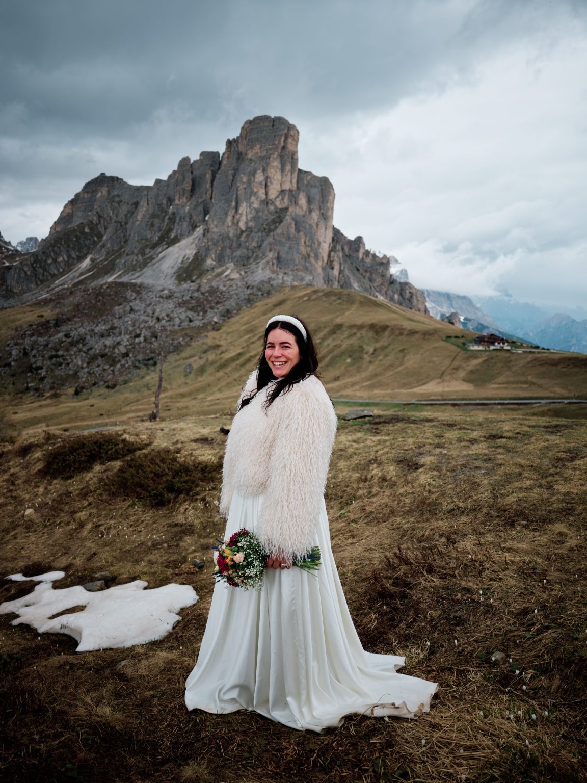 Elisa holding a bright bouquet at Passo Giau, green pastures and Dolomites peaks behind