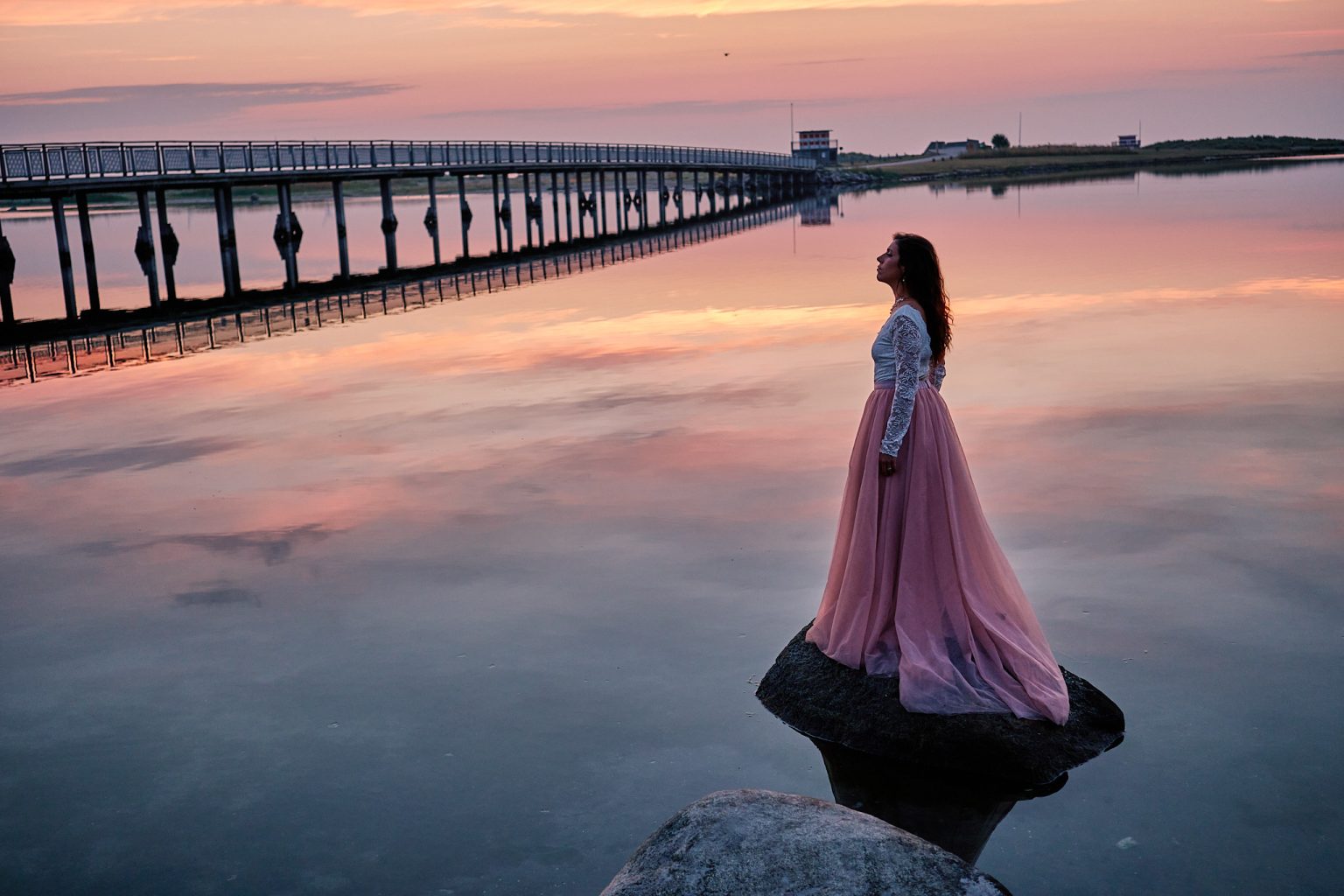 Irene standing in mirror-still shallows with a long pier behind, Copenhagen