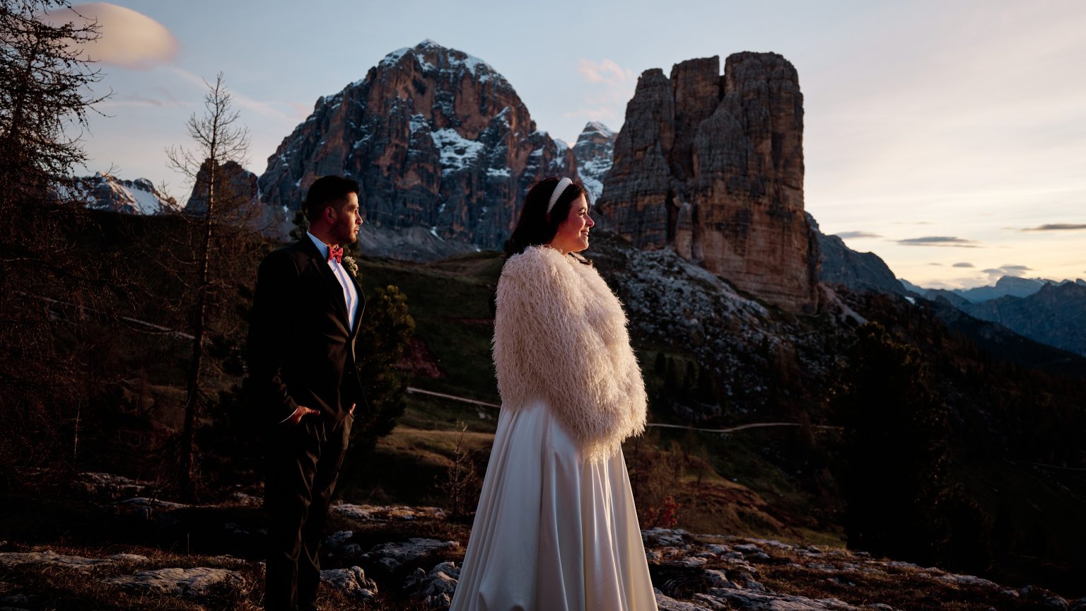 Elisa and Hector embracing in front of the Cinque Torri towers in warm sunrise light