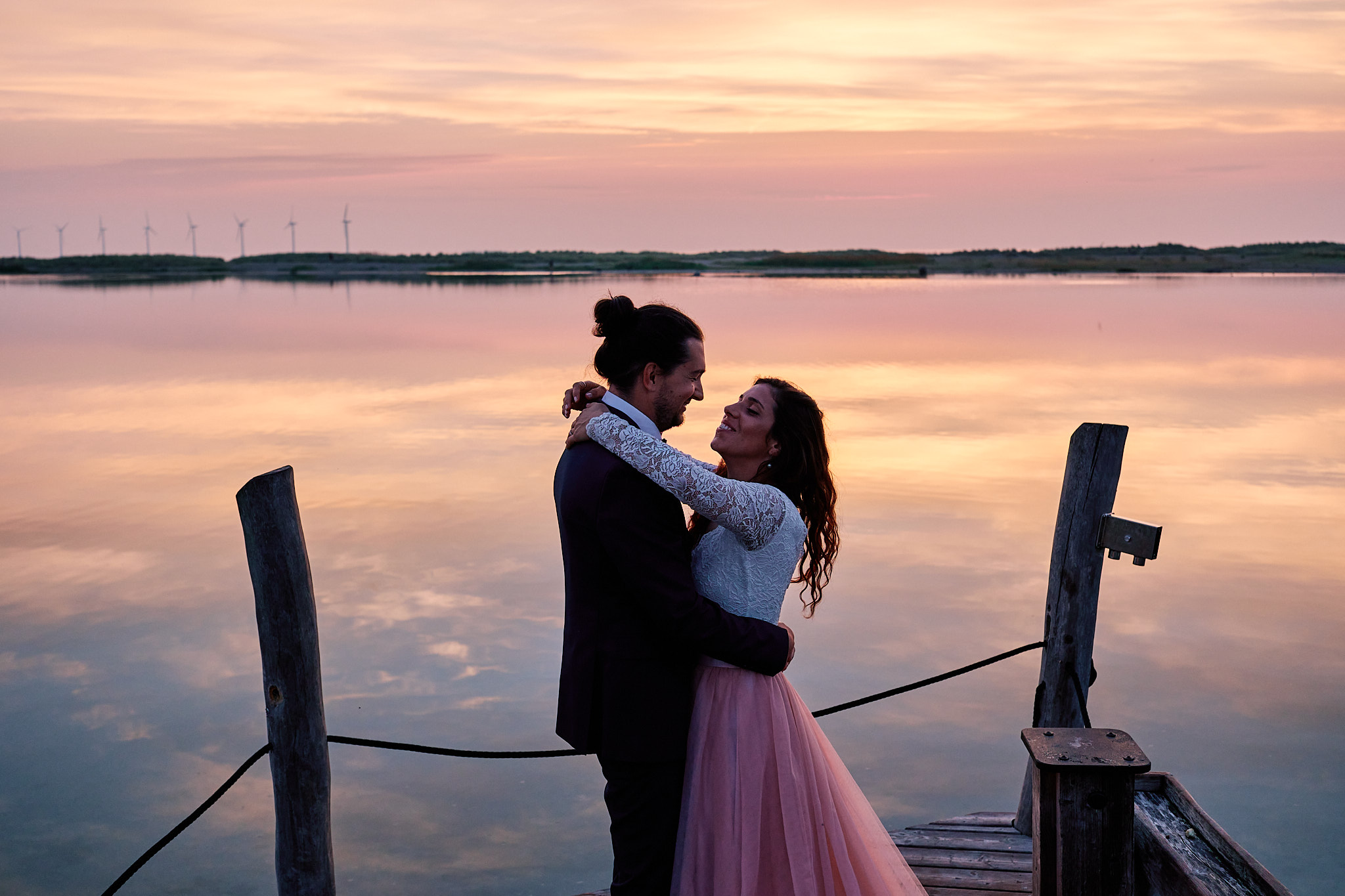 Irene and Jan embracing at a wooden pier railing at sunrise