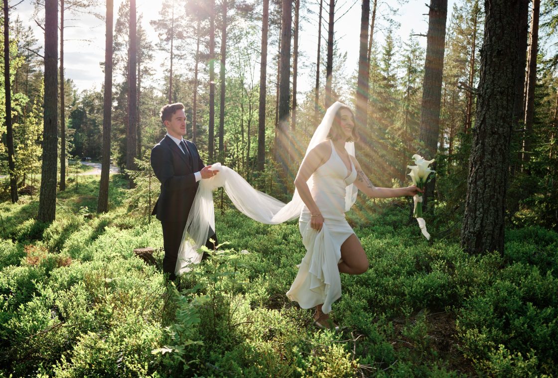Martin carrying Sara’s veil through the forest at Hop Farm Beach, a cabin elopement in Sweden