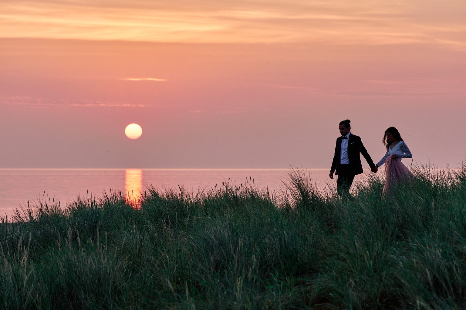 The couple walking the dunes as the sun climbs over the sea near Copenhagen
