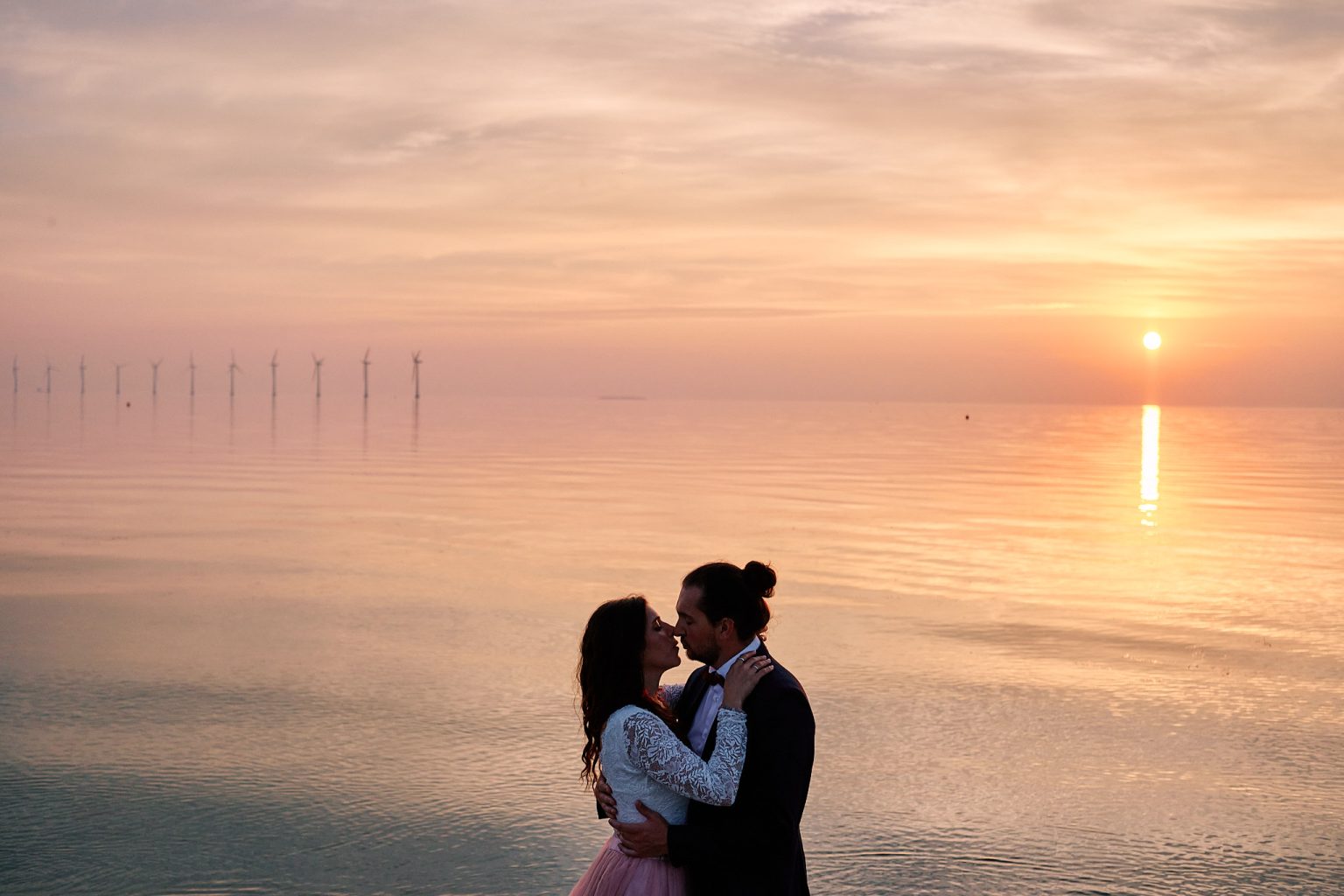 The couple small against the pastel sea with wind turbines on the horizon, Copenhagen