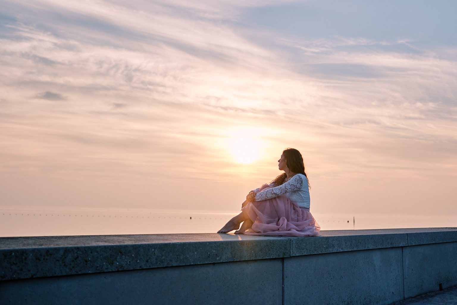 Irene in a pink dress sitting on the seawall at sunrise, Copenhagen elopement session