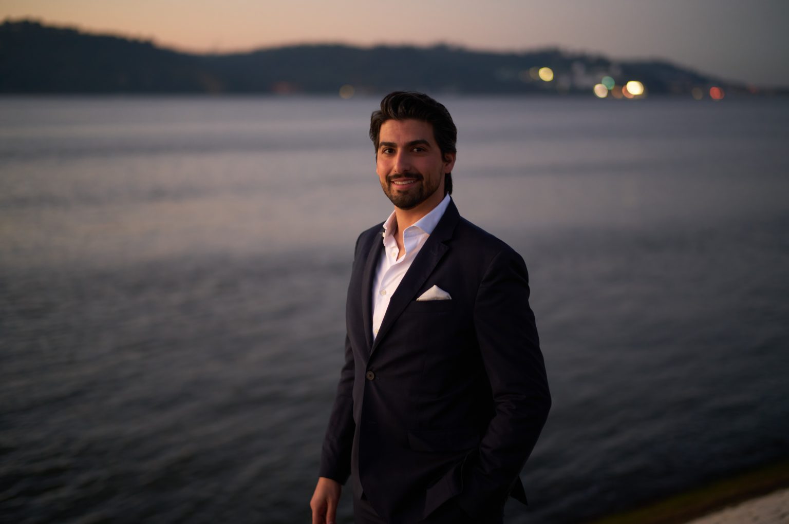 David in a navy suit on the Lisbon waterfront at dawn