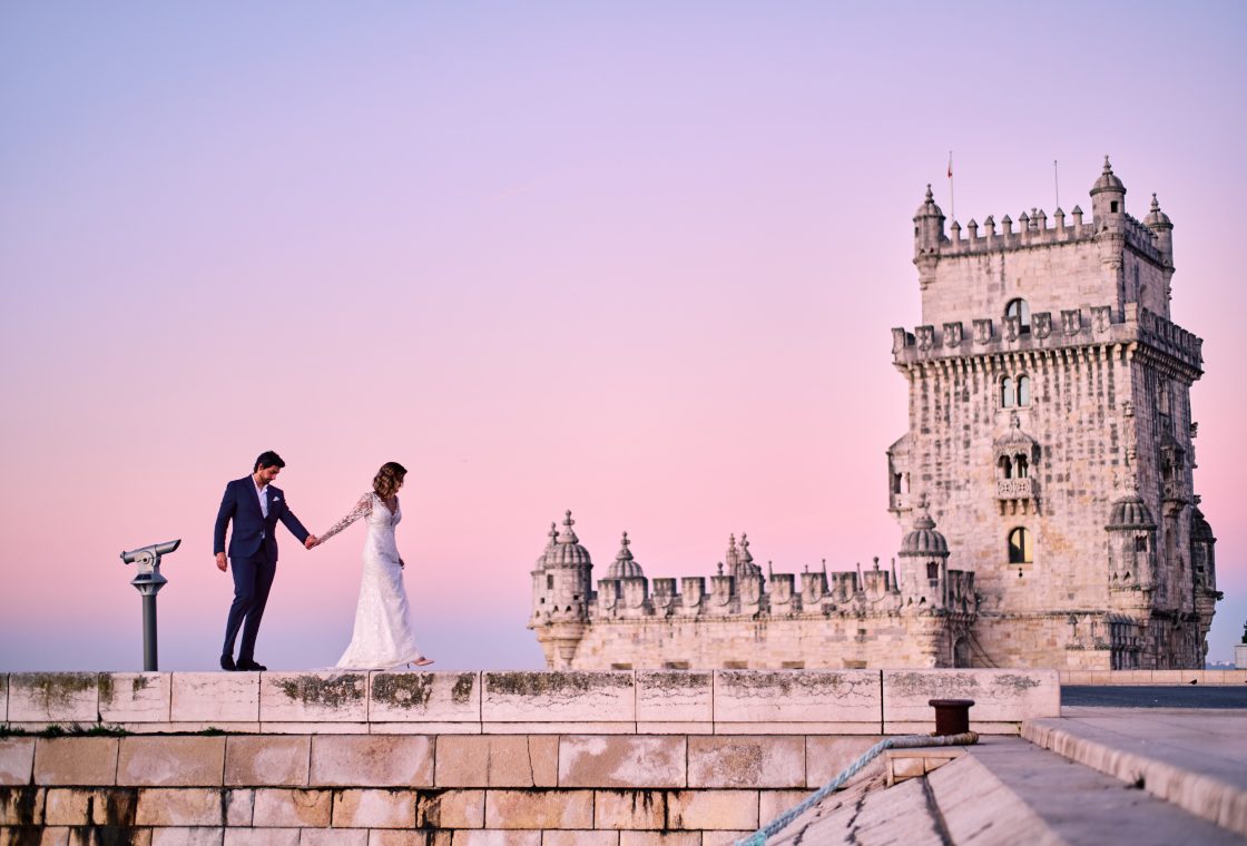 Ana and David holding hands in front of the Torre de Belém at sunrise, Lisbon elopement session