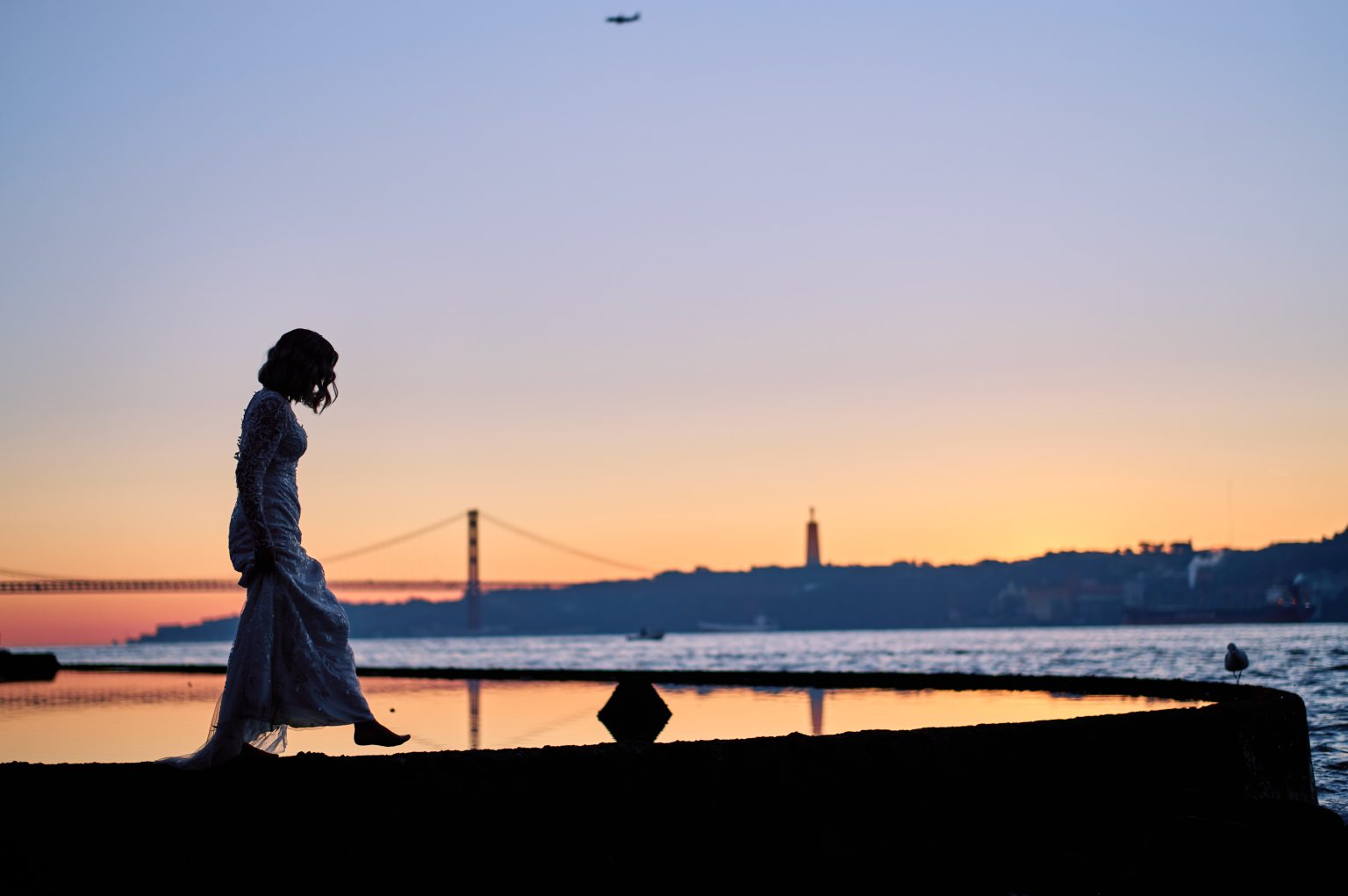 Ana walking the seawall in Belém with the 25 de Abril bridge in the distance