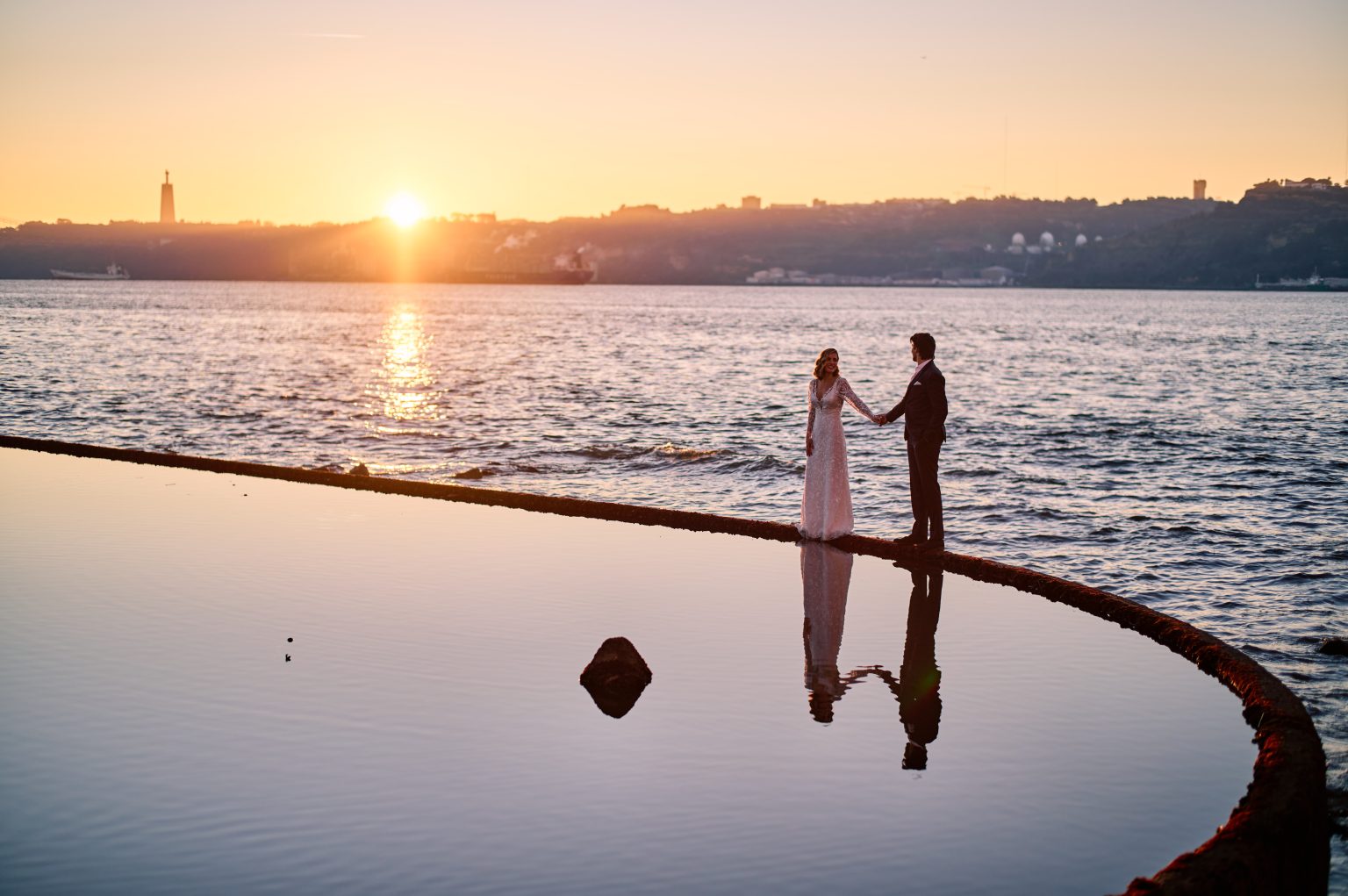 Ana and David reflected in the pool beside the Tejo river at sunrise in Lisbon