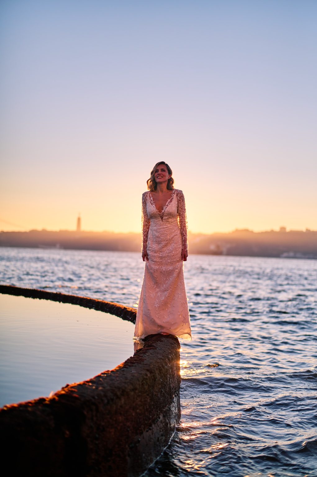 Ana backlit by the rising sun over the Tejo during a Lisbon elopement session