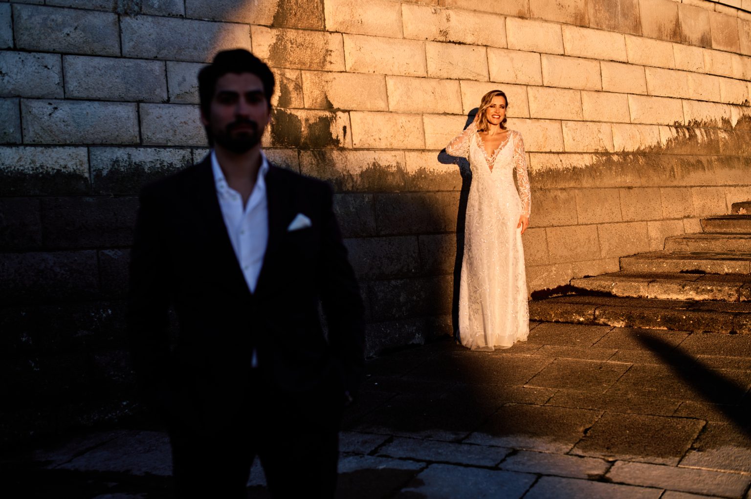 Ana and David against the fortress wall in hard morning light in Belém