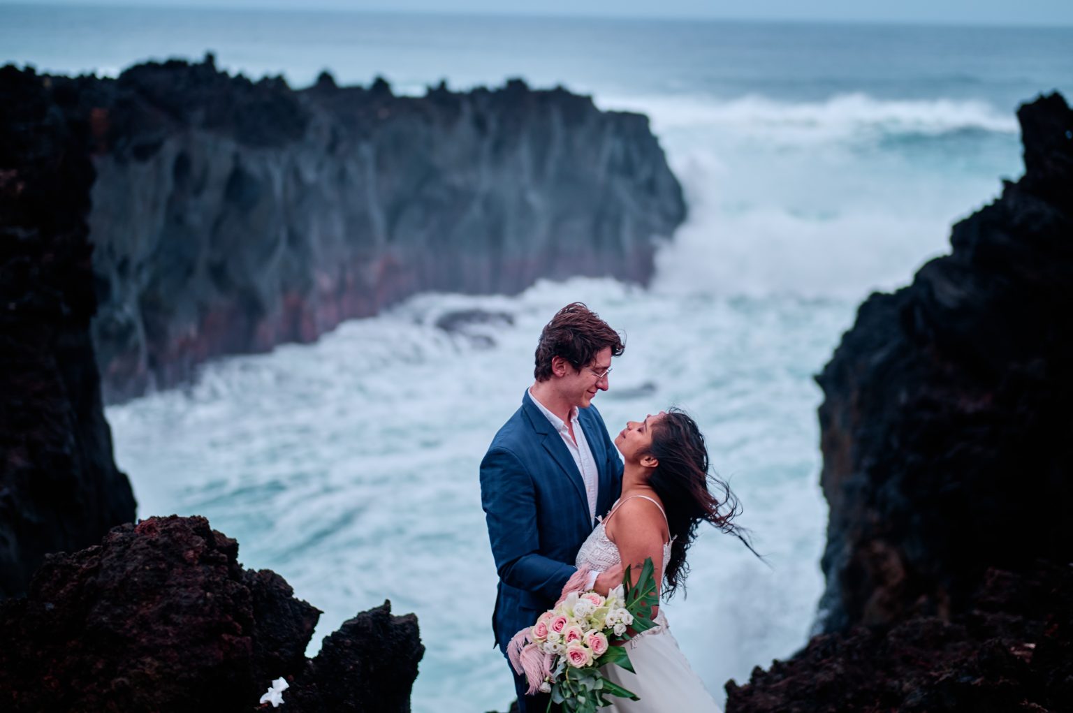 Couple on the black lava rocks at Ponta da Ferraria as the surf crashes, São Miguel