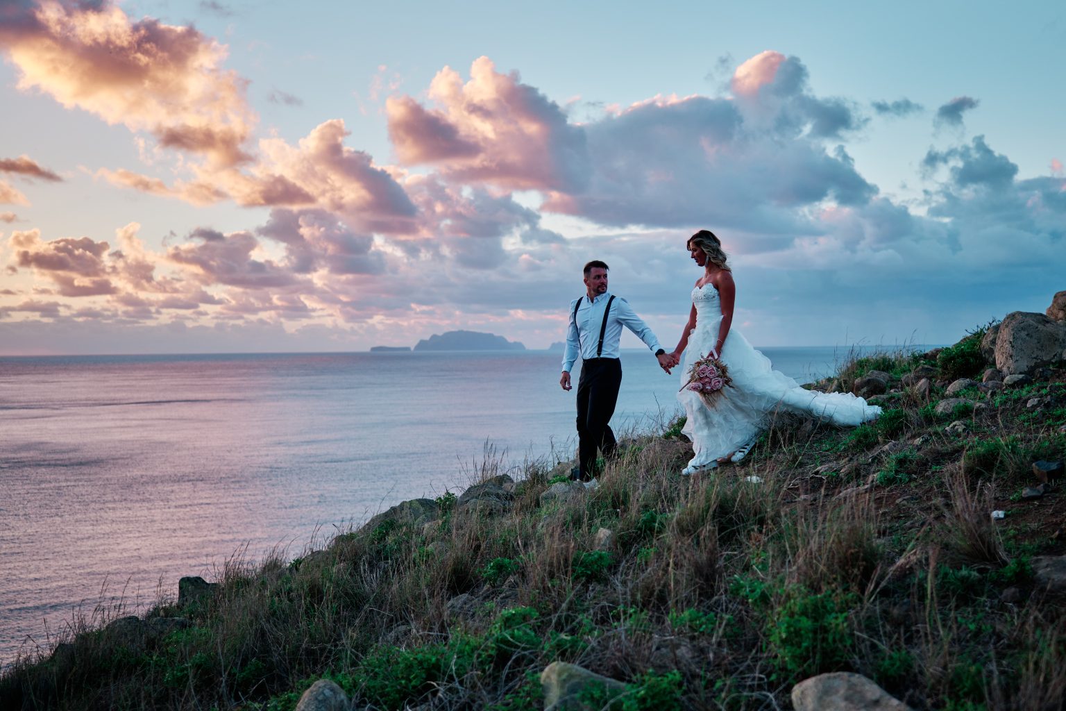 Couple holding hands on a green clifftop at pastel dawn, Ponta de Sao Lourenco, Madeira