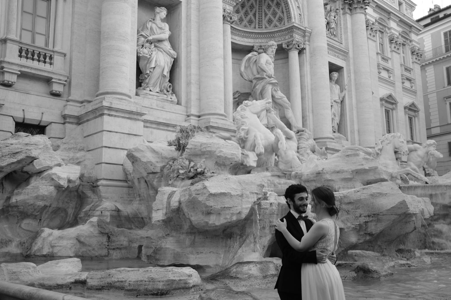 The couple embracing at an empty Trevi Fountain at dawn