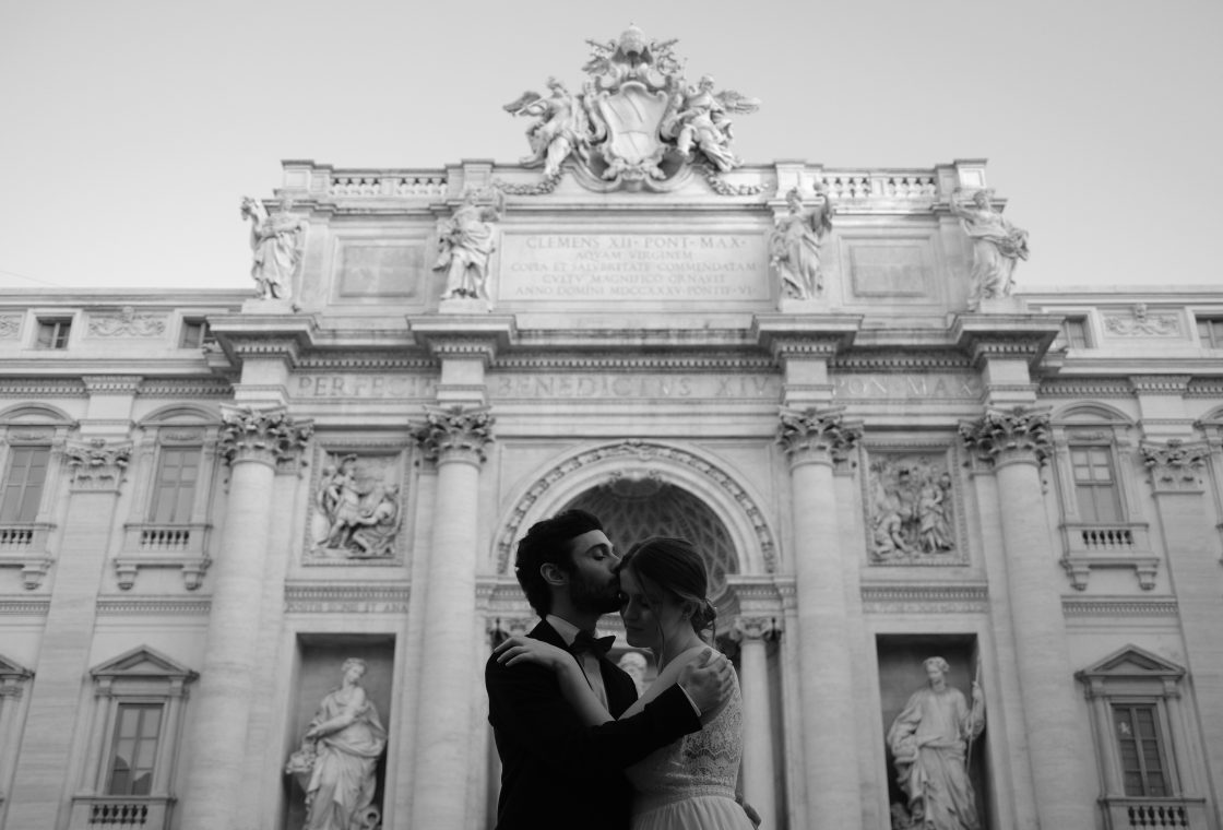 Rozina and Salvatore kissing before the Trevi Fountain facade at dawn, Rome engagement session in black and white