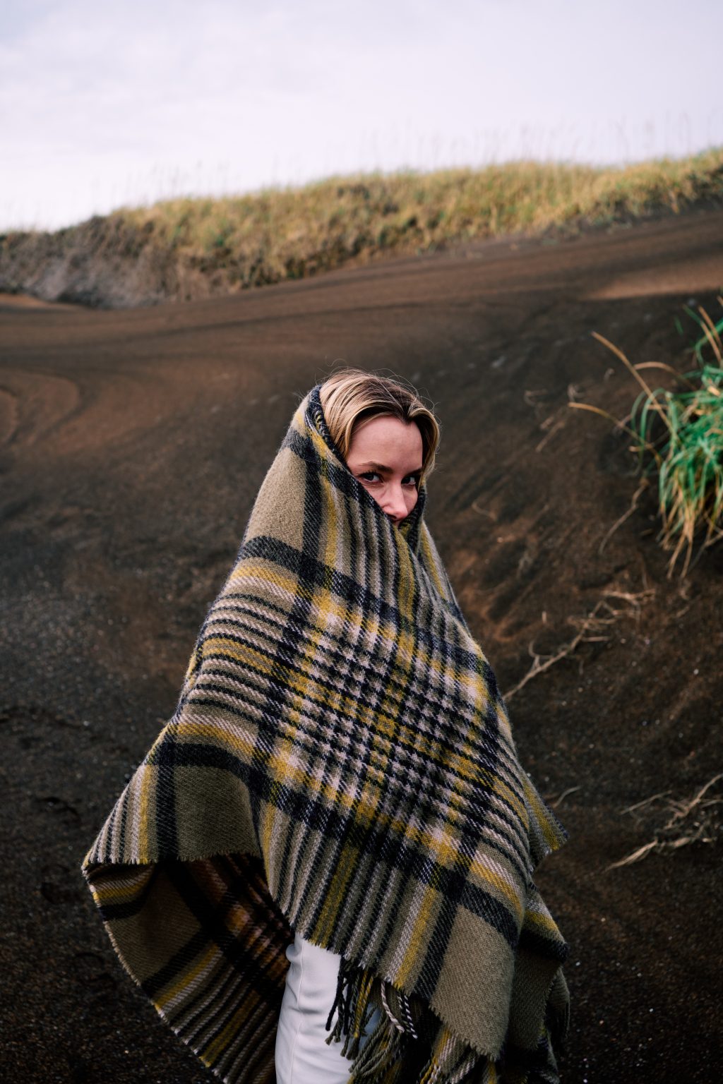 Bride wrapped in a wool blanket among the black dunes