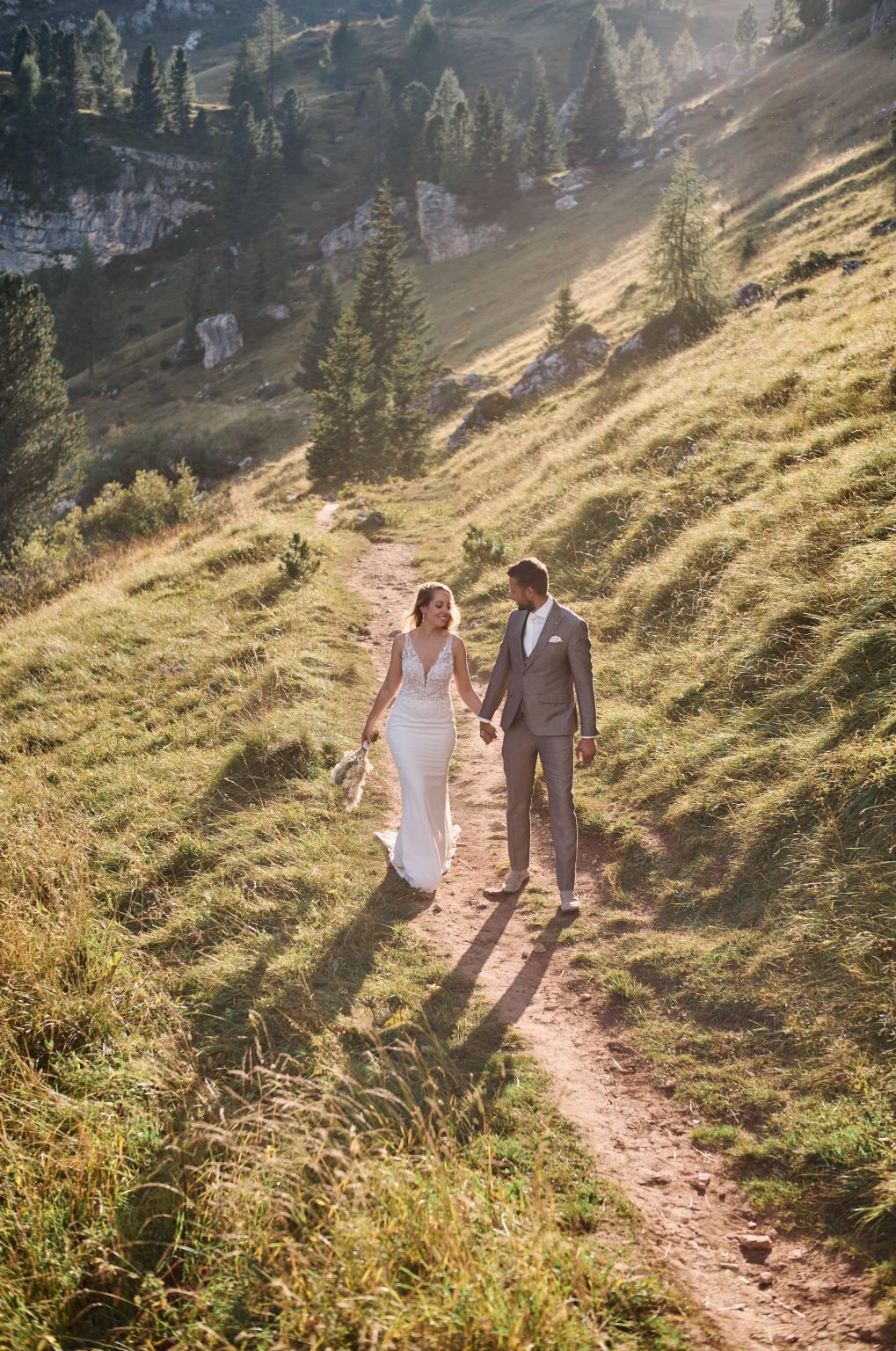 The couple climbing a green slope in the afternoon light, Dolomites wedding