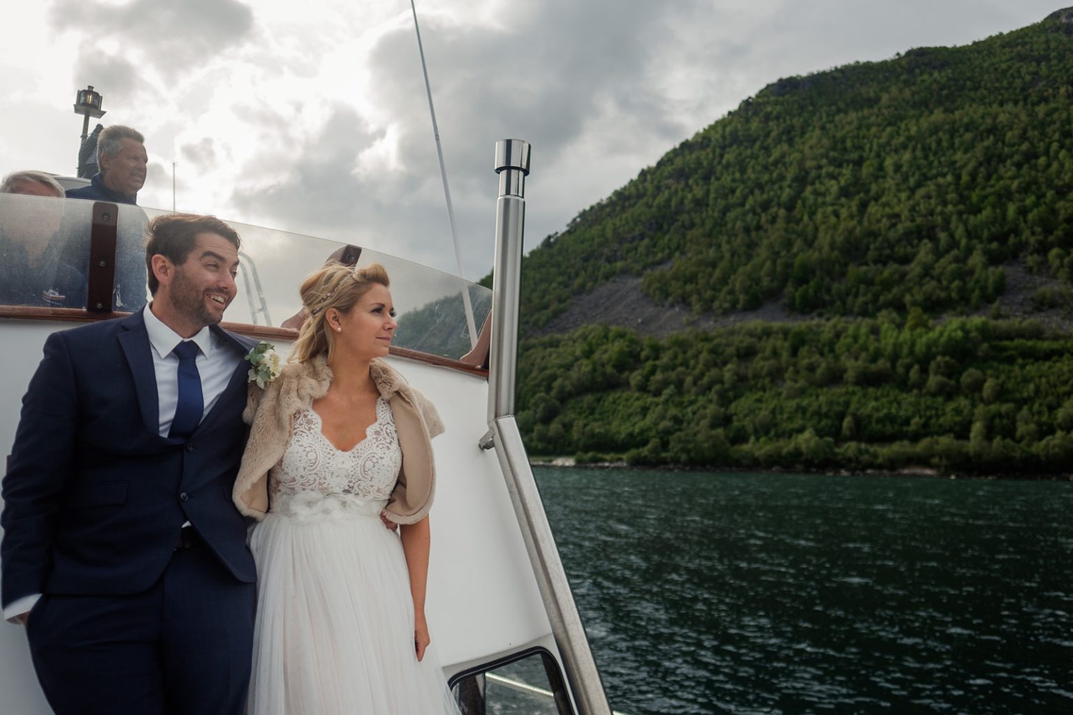 Bride and groom on deck with the fjord mountains behind