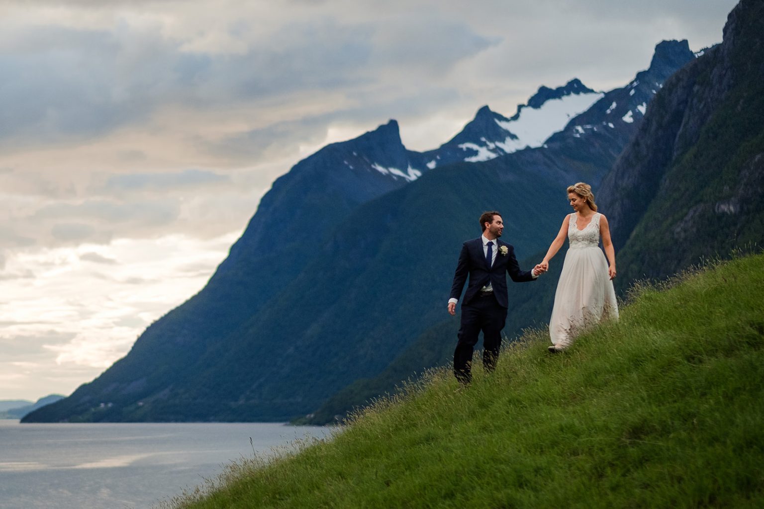 Bride and groom walking the green slope above the Hjørundfjord