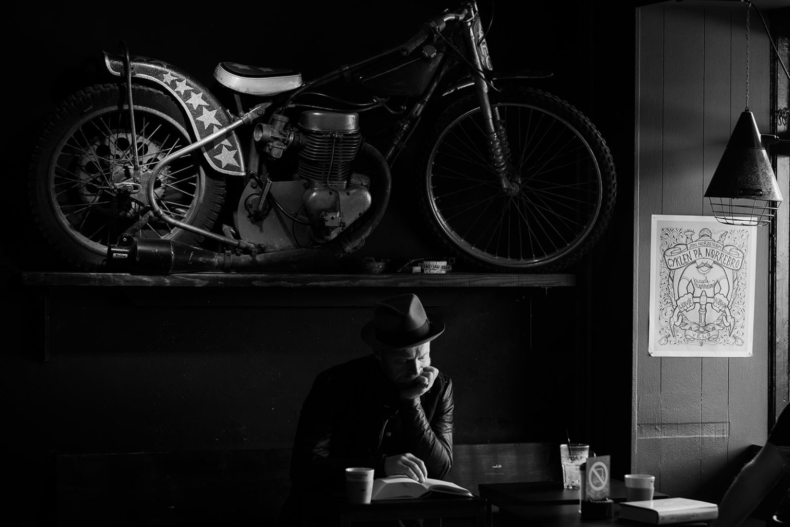 A stranger in a hat beneath an old motorcycle in a Copenhagen cafe