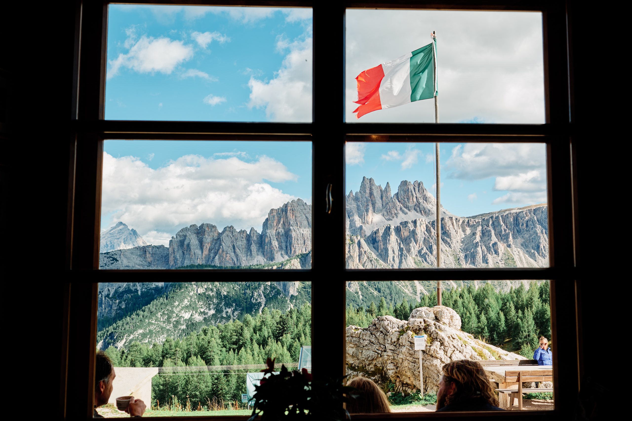 Rifugio window — Italian flags and Dolomites peaks