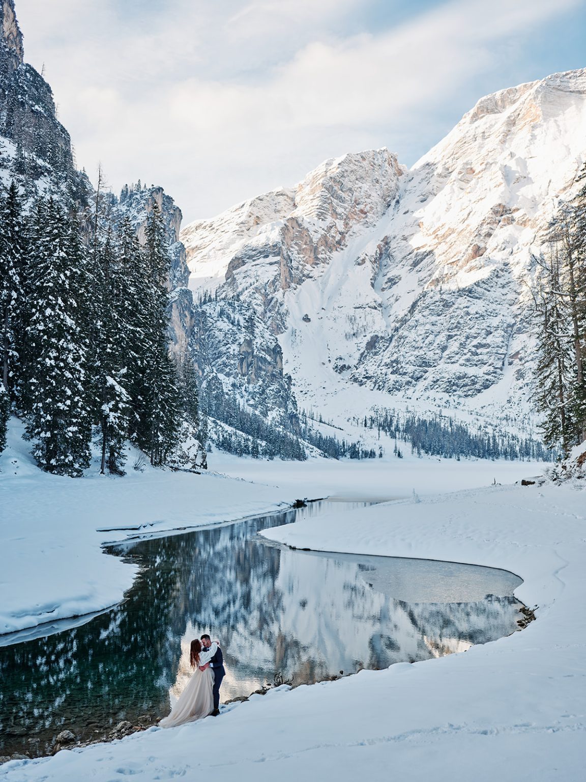 The couple tiny on the frozen lake below the peaks, the Dolomites in winter