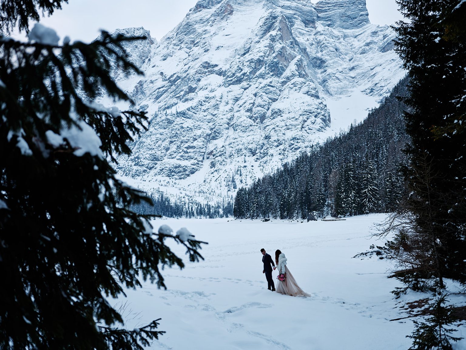 The Braies valley under snow, the couple tiny in the trees, Dolomites winter elopement