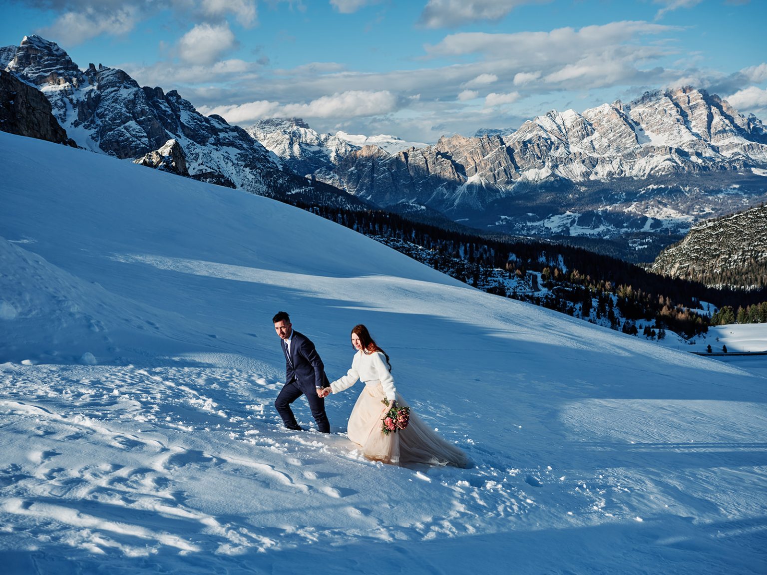 The couple crossing the snowfields with the Dolomites behind, Passo Giau