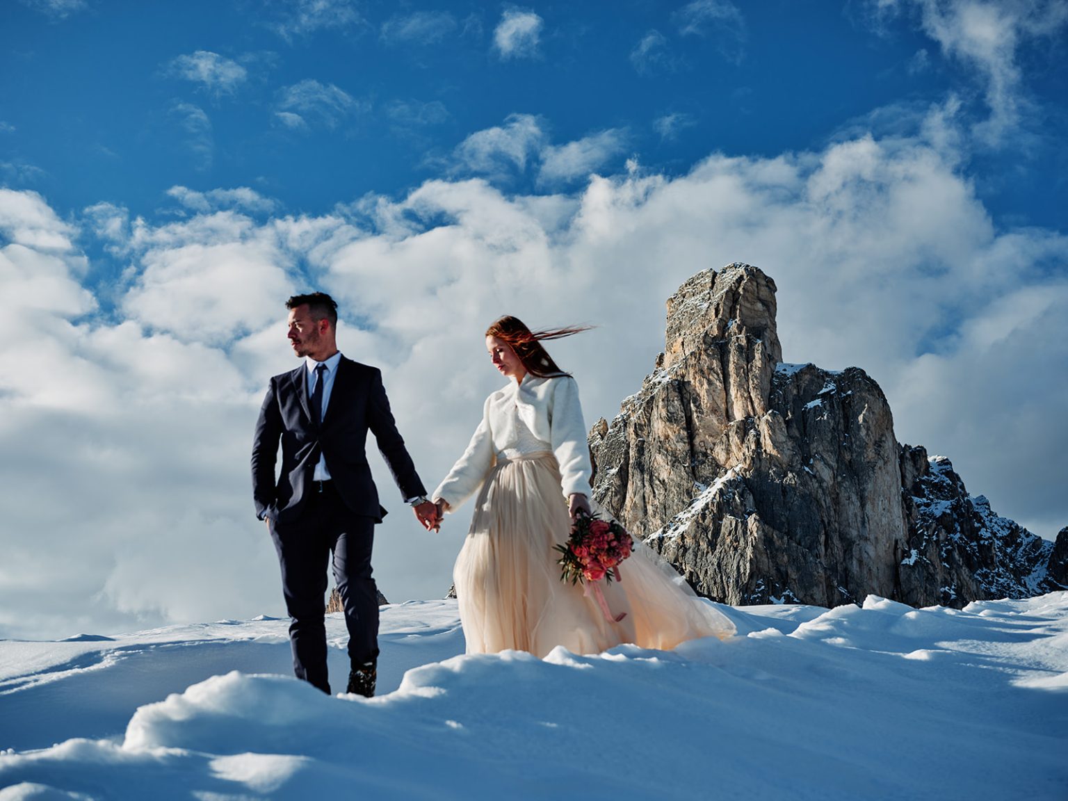 The couple walking the ridge below the towers, a Dolomites winter elopement