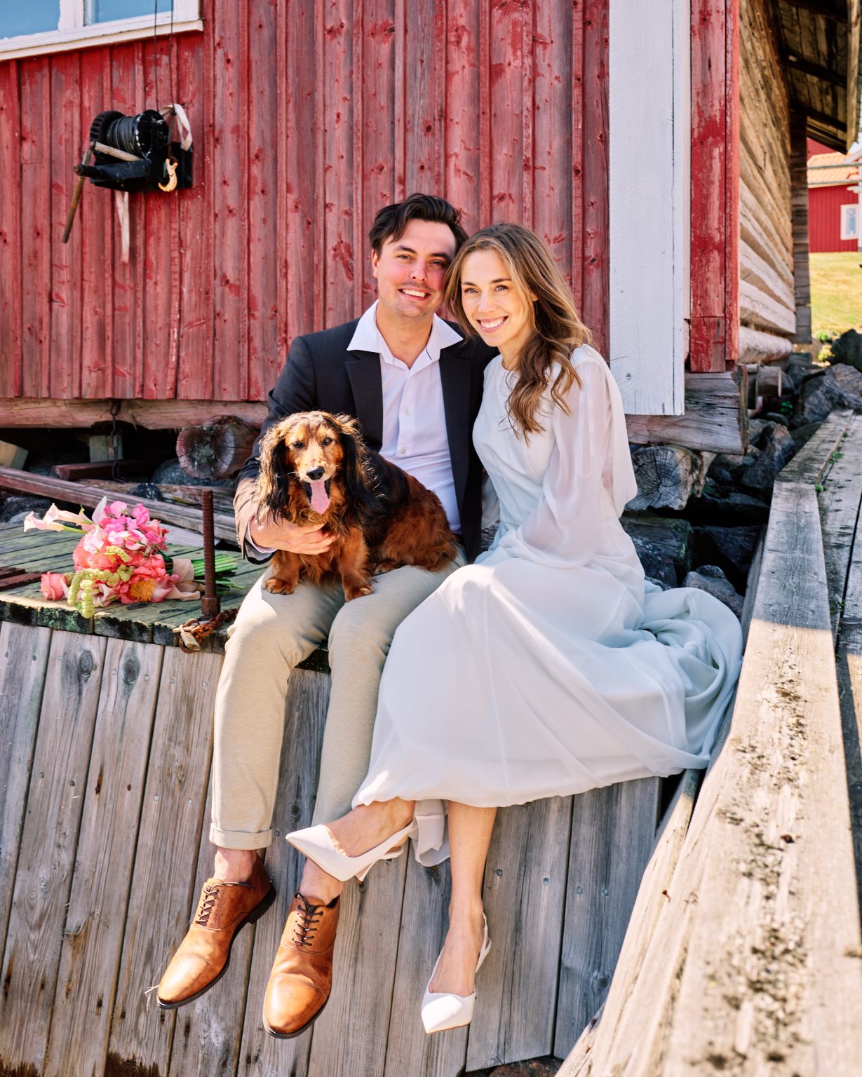 Elopement couple and their spaniel beside a red barn near Skärså
