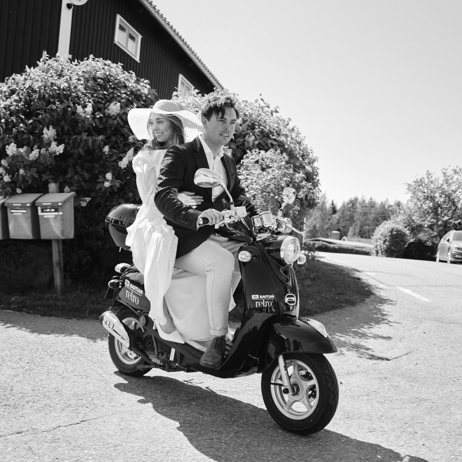 Elopement couple on a moped beside a red building, Skärså