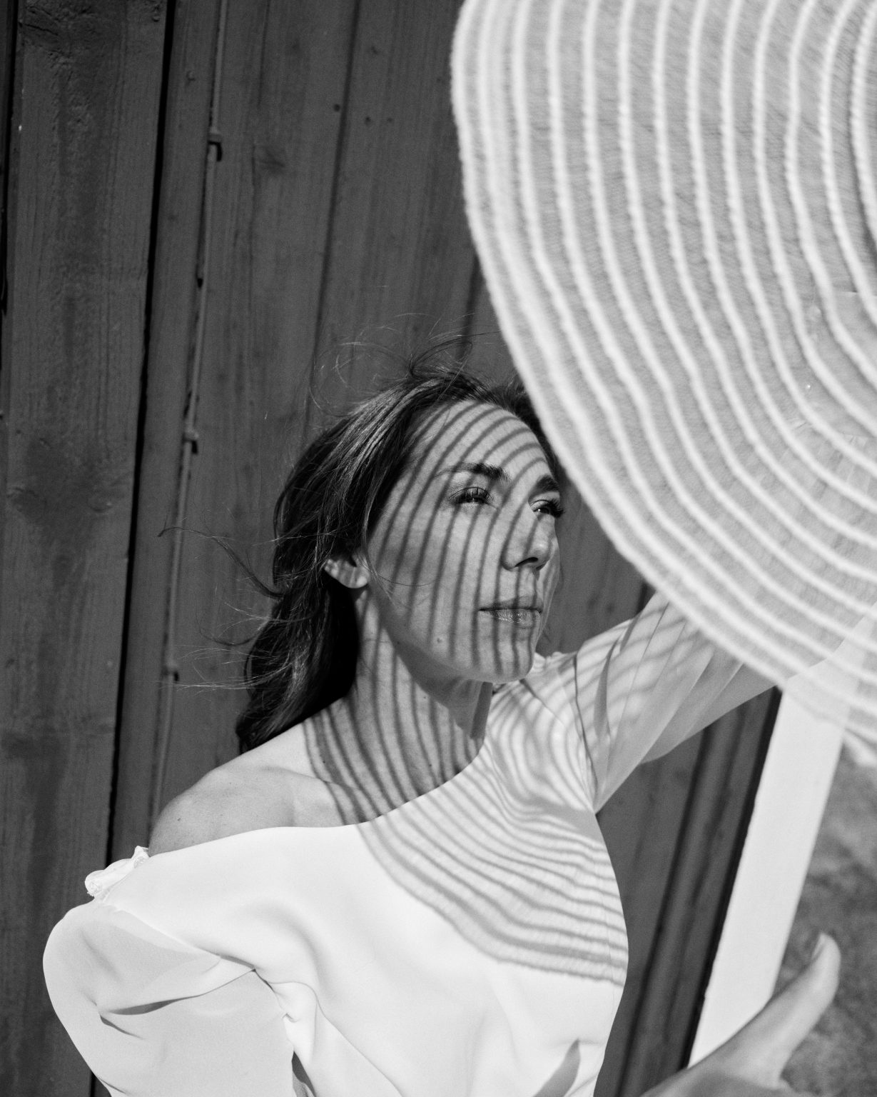 Editorial portrait of Elin in a wide-brimmed hat against a barn wall
