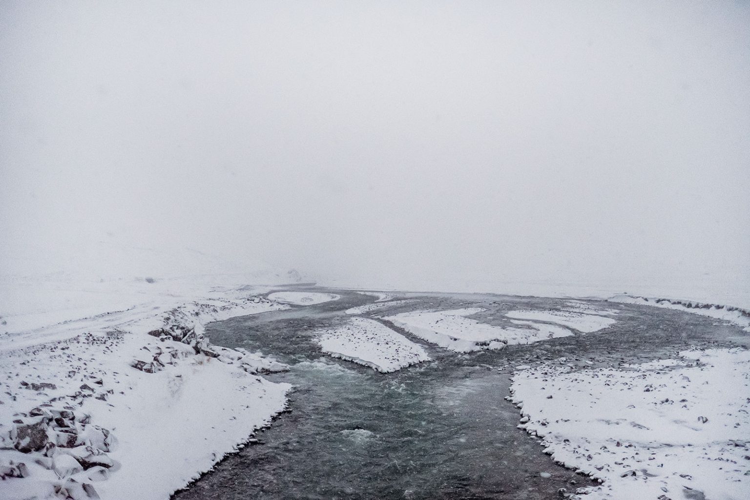A dark river running through the snow in Hvalfjörður