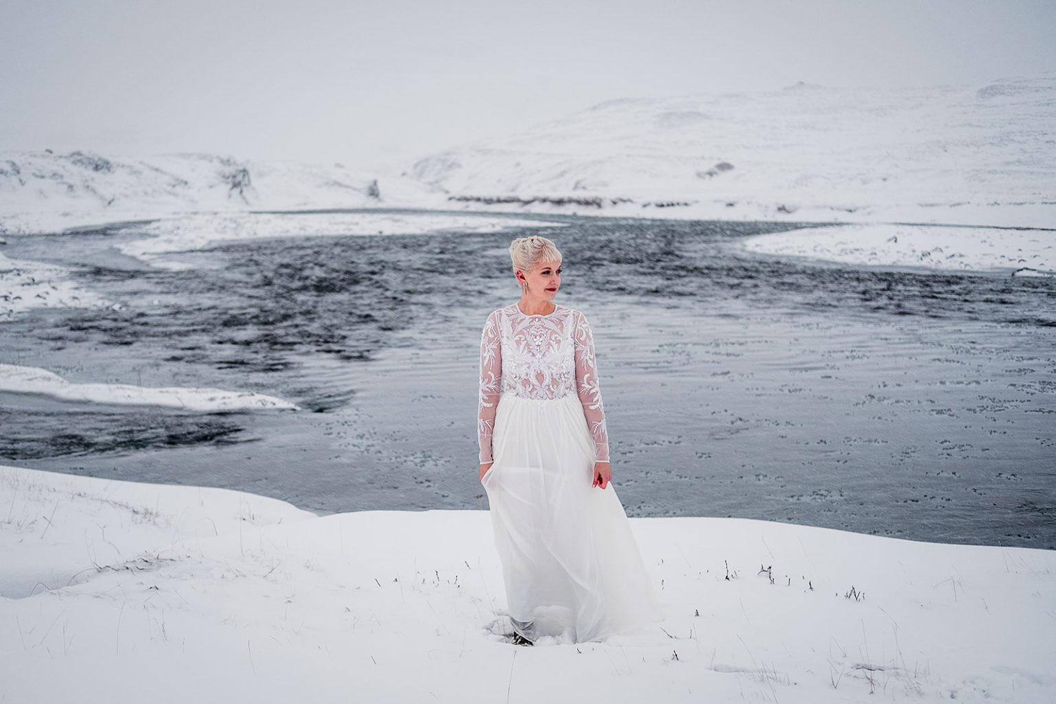 Bride crossing the snow toward the water in Hvalfjörður
