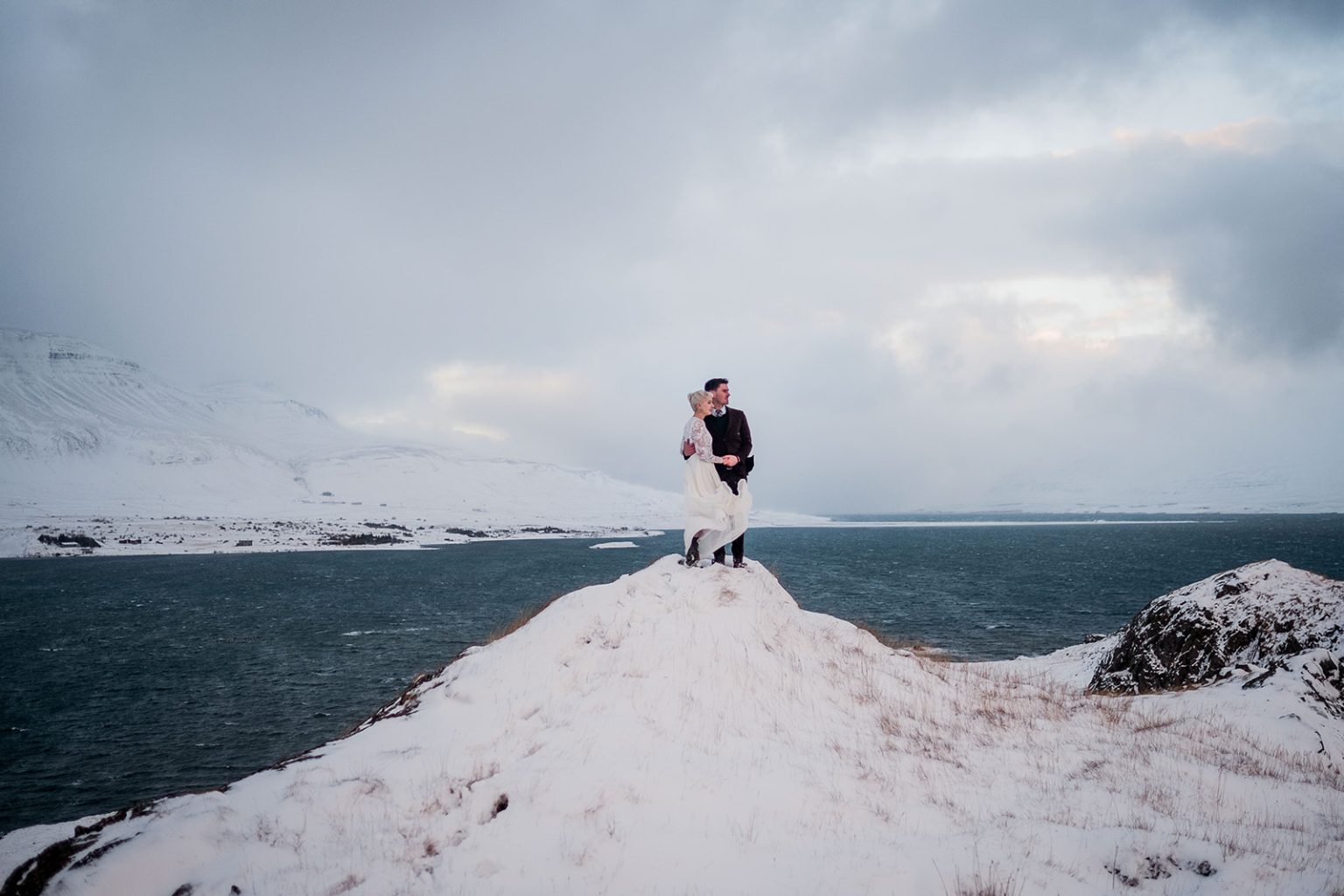 Bride and groom on a snow-covered rise above the fjord