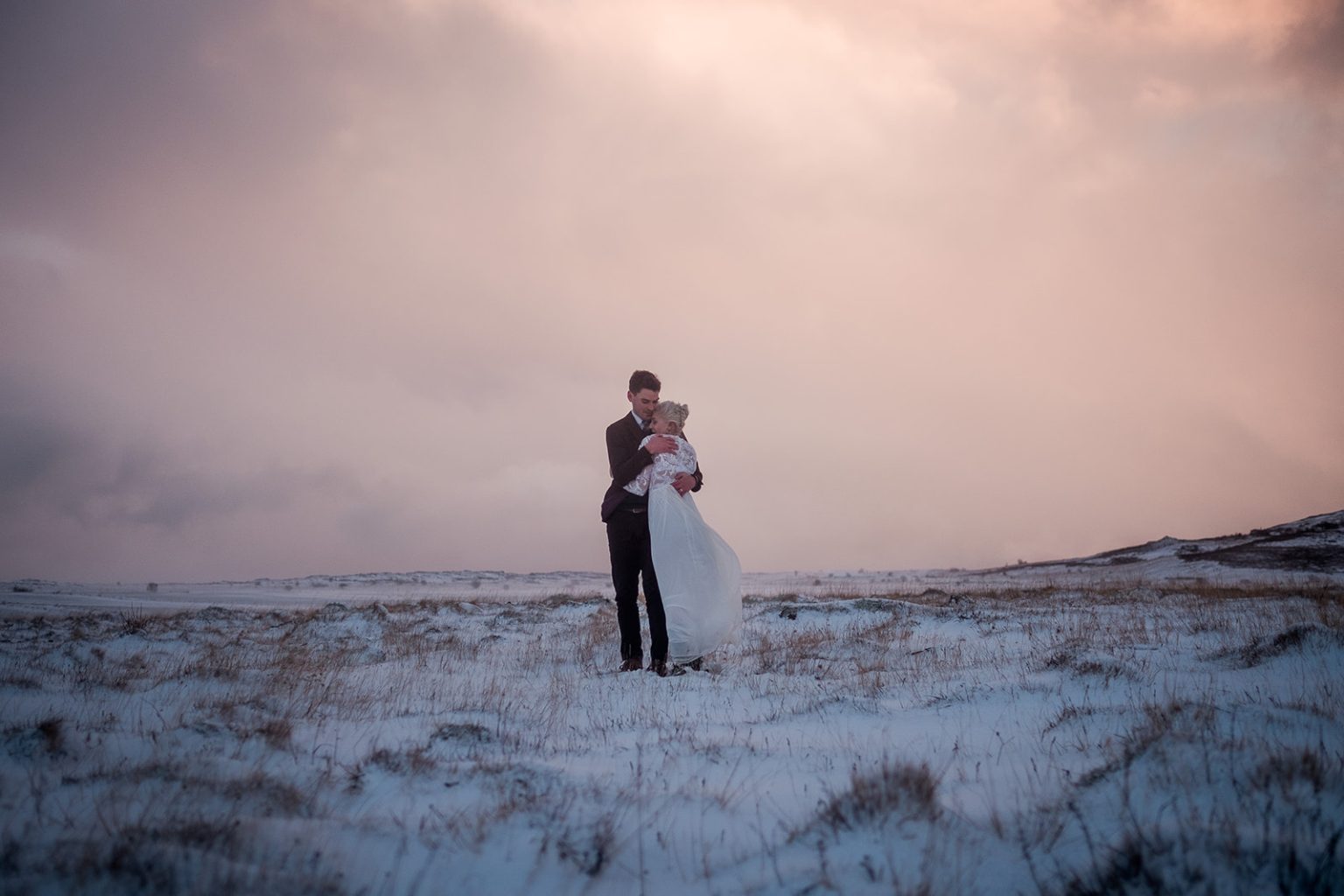 Bride and groom in soft pink winter light above the fjord