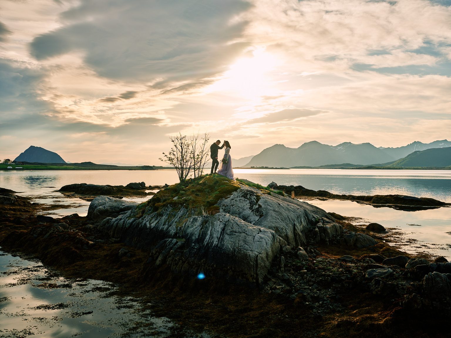 Sophie and Johan in silhouette on a Lofoten shore at sunset