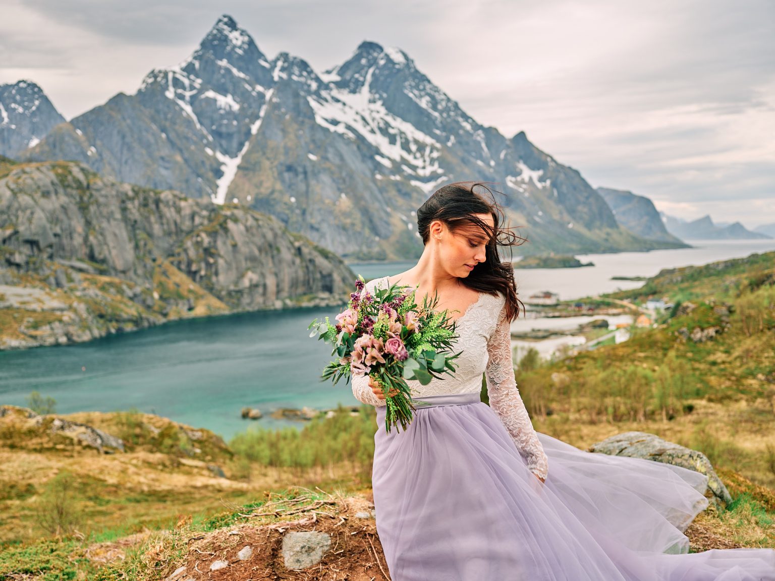 Bride with her bouquet above a turquoise Lofoten fjord