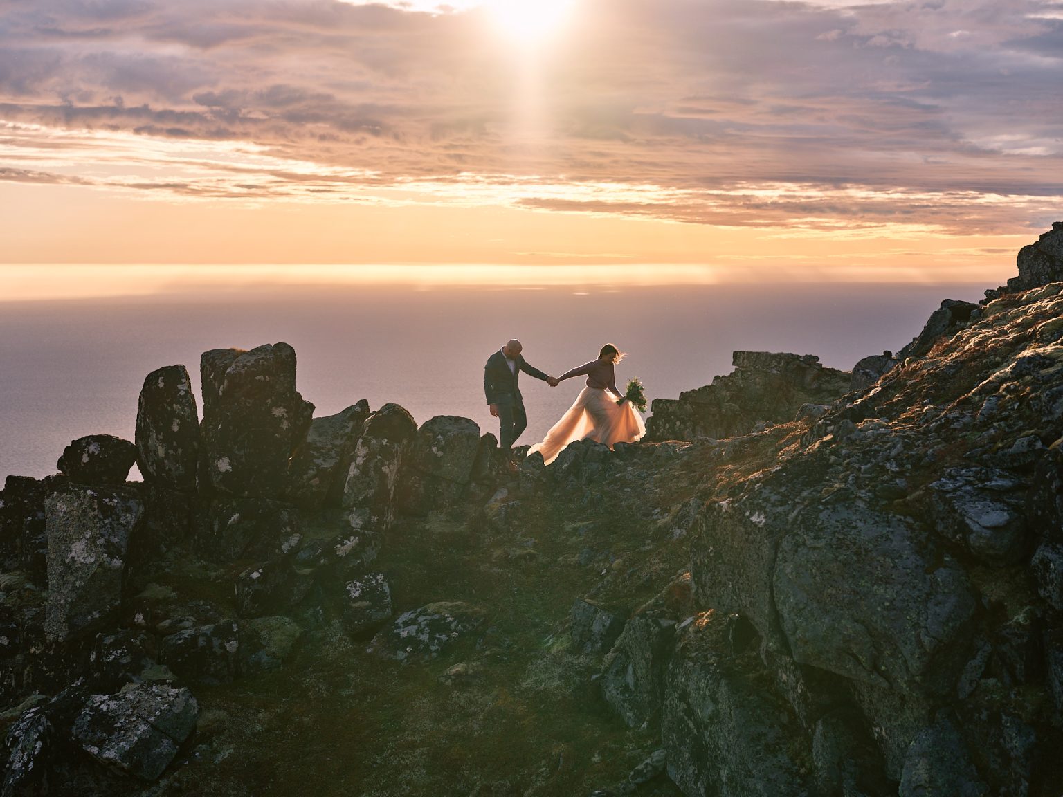 Ine and Jimmy on the rocks at sunset above the sea, Lofoten