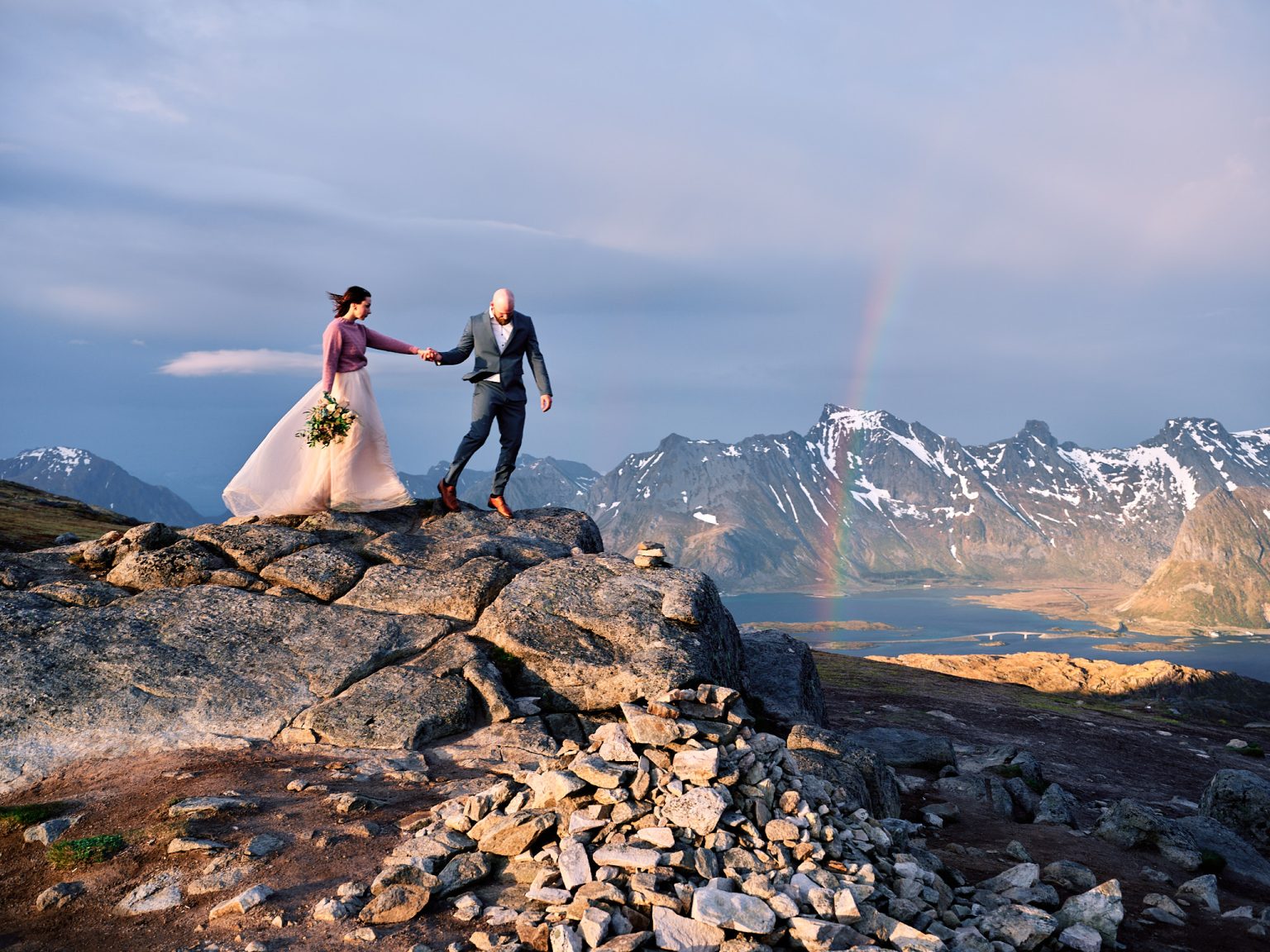 A rainbow over the peaks as the couple stand on the ridge, Lofoten