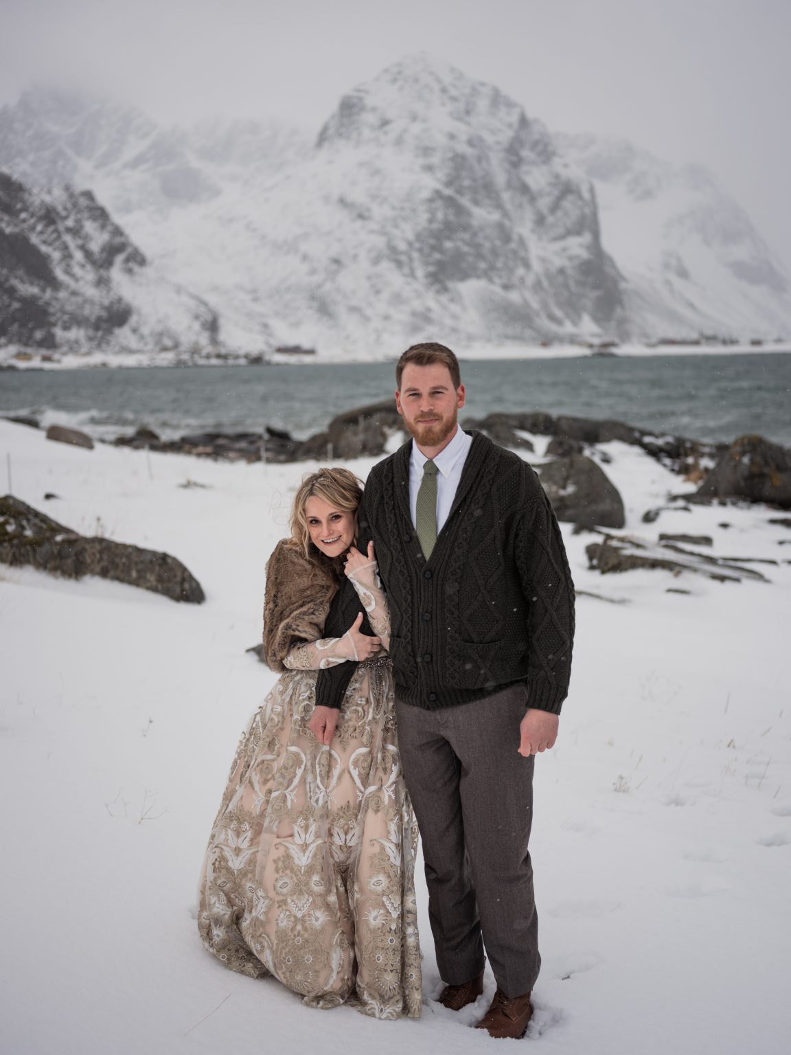 Jamie and Christopher in the snow below the mountains, elope in Lofoten