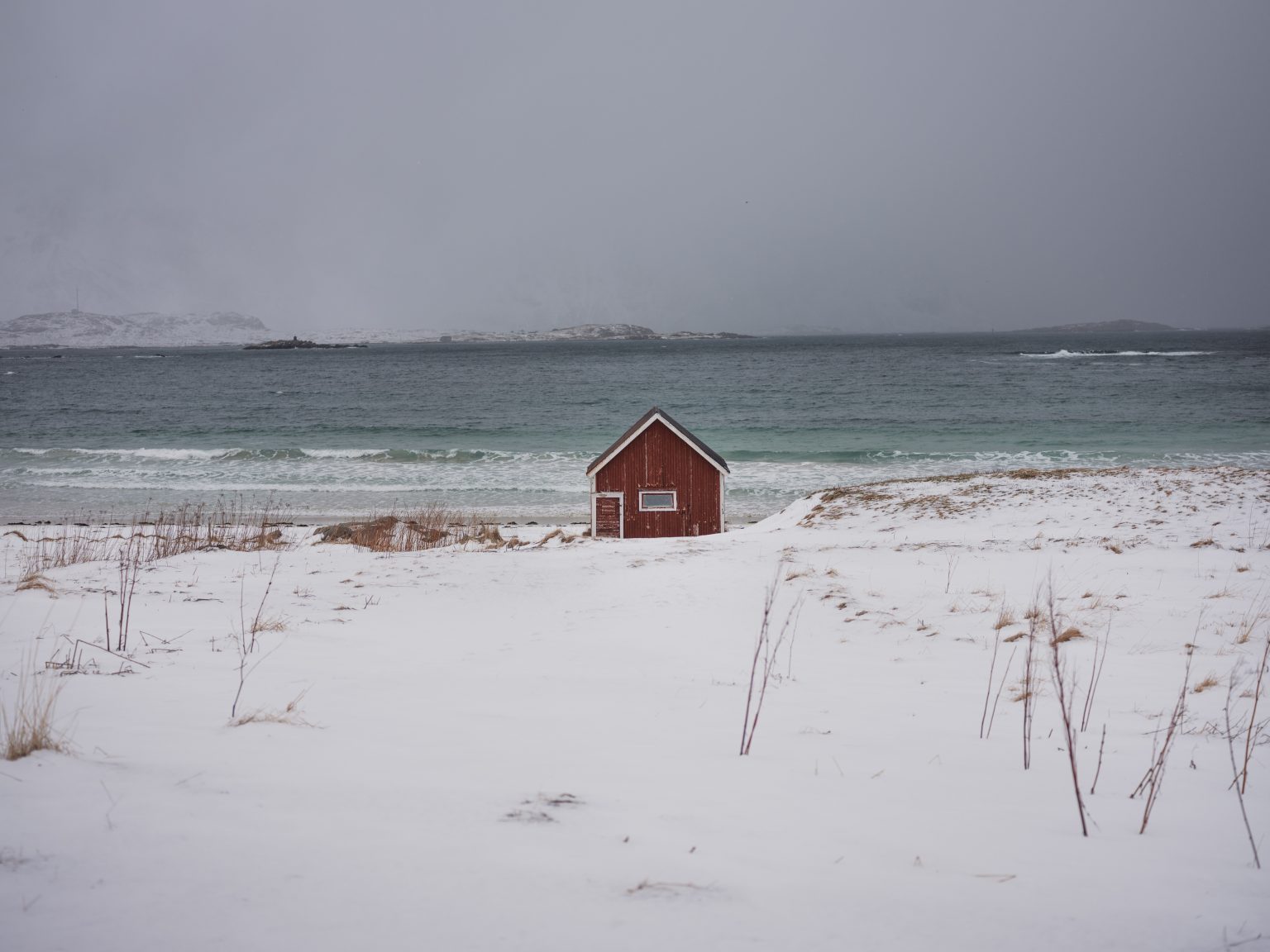 A lone red cabin below vast snowy mountains, Lofoten