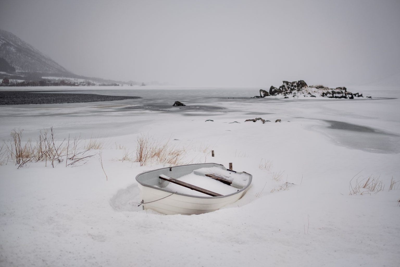 A boat on a snowy shore below the mountains, winter in Lofoten